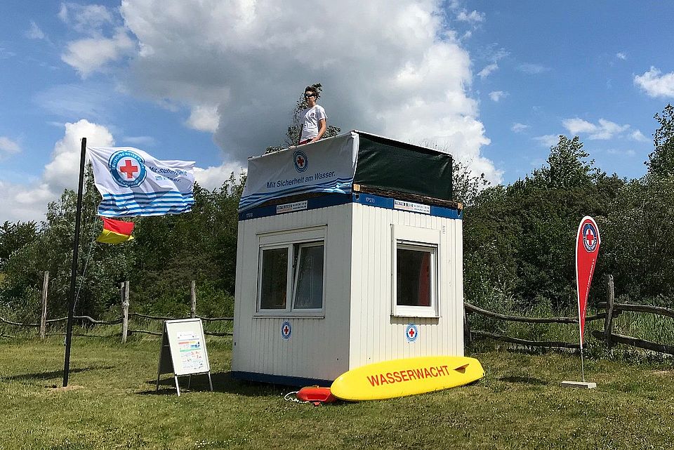 Rettungsschwimer steht auf Wachcontainer mit Wasserwachtflaggen